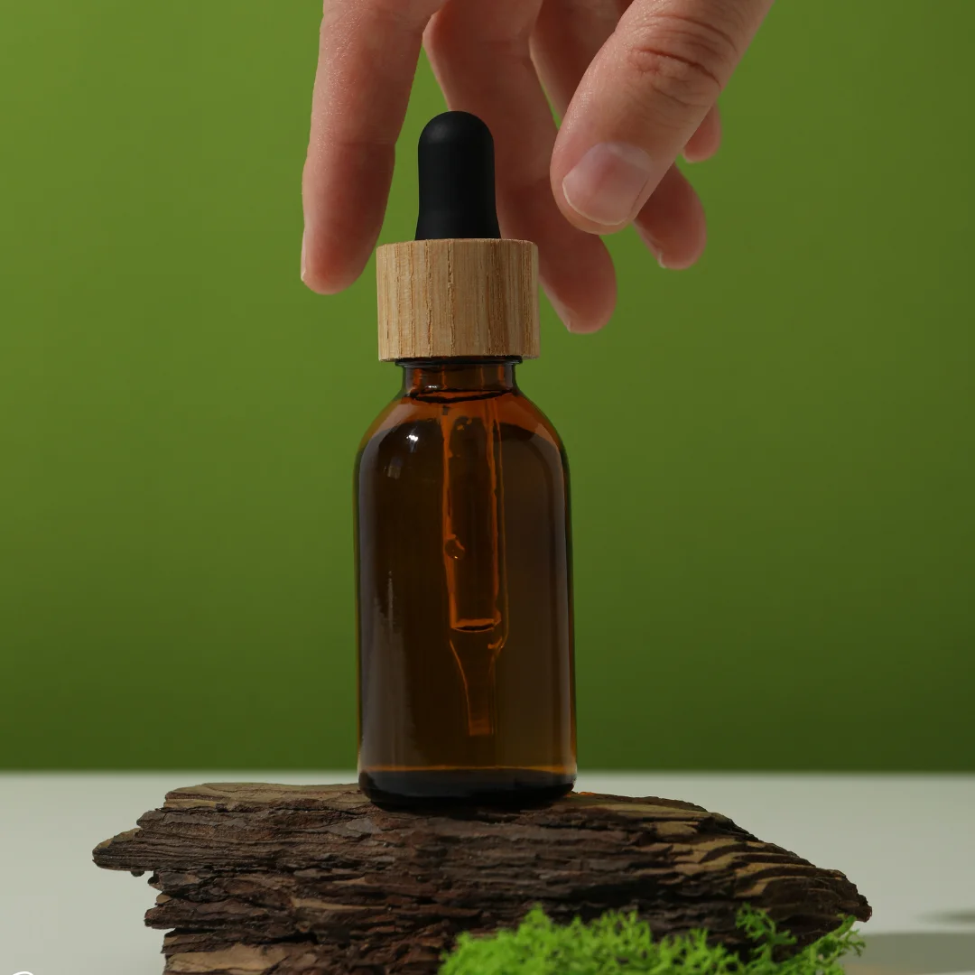 Amber dropper bottle of pure eucalyptus essential oil displayed on wooden bark with natural green background.